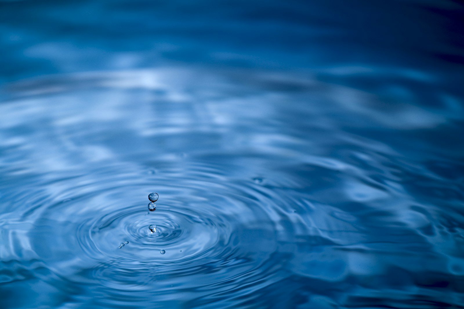 A water drop falling into calm blue water, sending out ripples